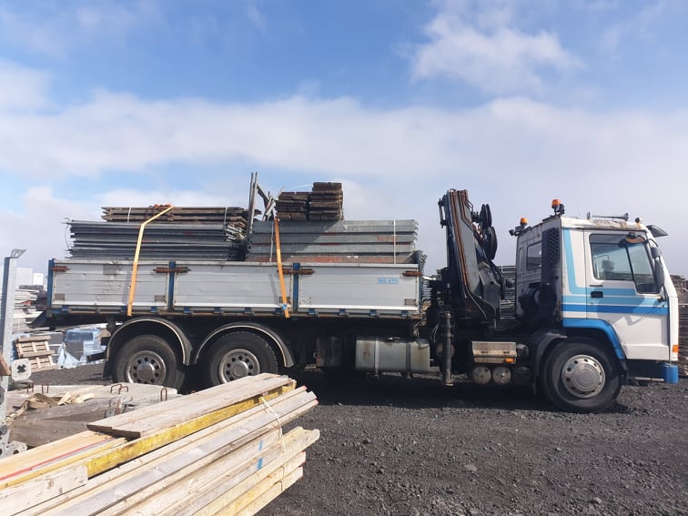 Vörubíll með krana hlaðinn efni á verkstað.